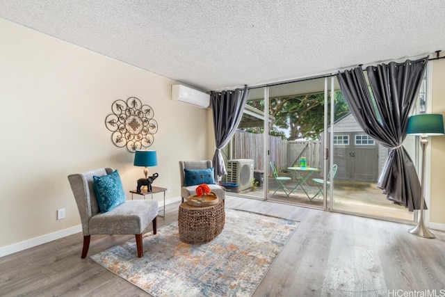 living area featuring a textured ceiling, wood finished floors, a wall of windows, a wall mounted air conditioner, and baseboards