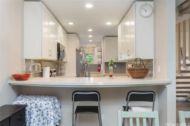 kitchen featuring white cabinetry, backsplash, stainless steel appliances, and a breakfast bar