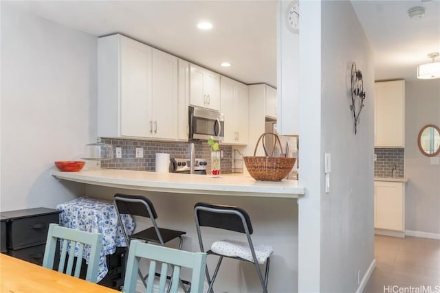 kitchen with a kitchen bar, white cabinetry, kitchen peninsula, decorative backsplash, and stove