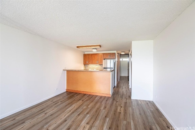 kitchen with tasteful backsplash, a textured ceiling, stainless steel fridge, kitchen peninsula, and light hardwood / wood-style floors