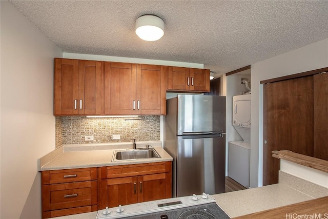 kitchen with stacked washer and dryer, sink, tasteful backsplash, a textured ceiling, and stainless steel fridge