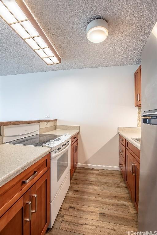 kitchen with white electric stove, sink, a textured ceiling, and light wood-type flooring