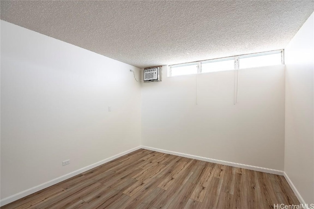 basement with a wall mounted air conditioner, hardwood / wood-style flooring, and a textured ceiling