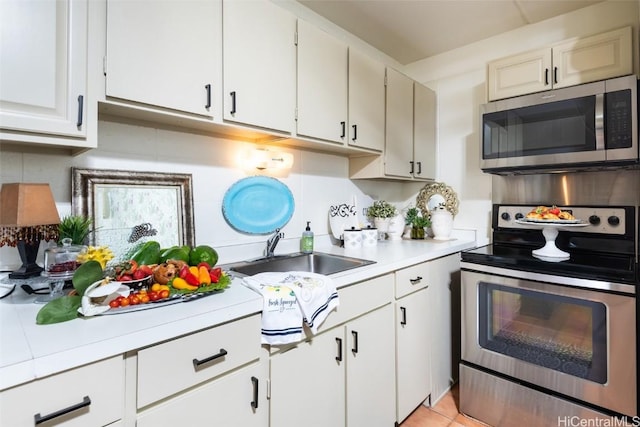 kitchen with white cabinets, decorative backsplash, appliances with stainless steel finishes, light countertops, and a sink