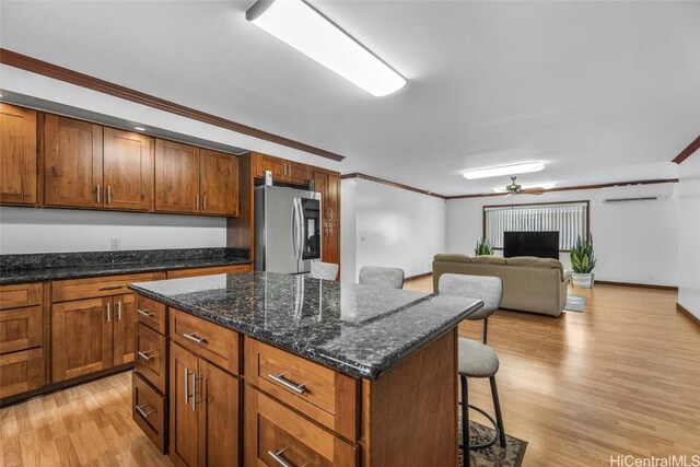 kitchen featuring crown molding, stainless steel fridge, a wall unit AC, light hardwood / wood-style floors, and a kitchen bar