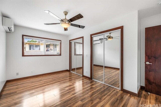 unfurnished bedroom featuring ceiling fan, a wall mounted AC, hardwood / wood-style floors, and two closets