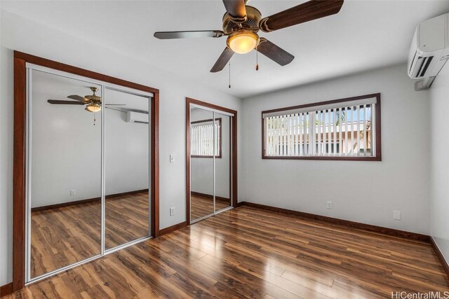 unfurnished bedroom featuring dark hardwood / wood-style flooring, two closets, an AC wall unit, and ceiling fan