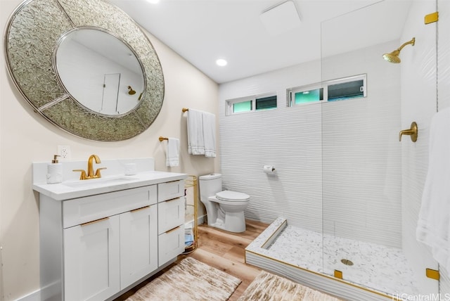 bathroom featuring hardwood / wood-style flooring, vanity, tiled shower, and toilet