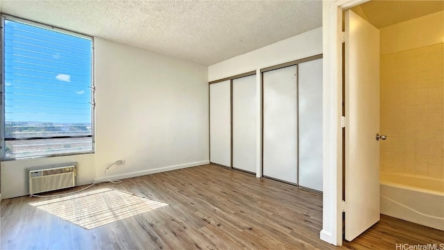 unfurnished bedroom with multiple closets, a wall mounted air conditioner, a textured ceiling, and light wood-type flooring