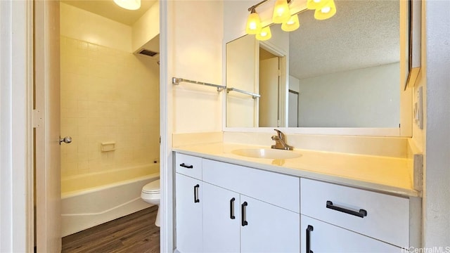 full bathroom featuring hardwood / wood-style flooring, vanity, tiled shower / bath combo, toilet, and a textured ceiling