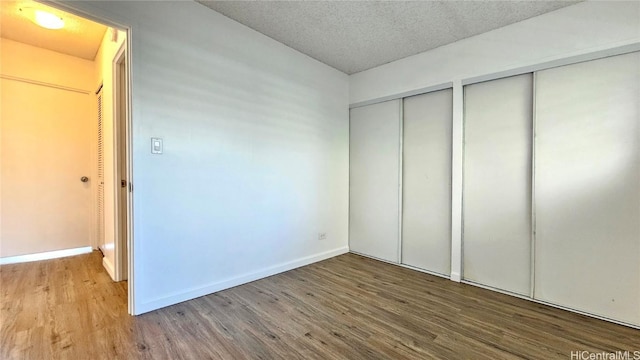 unfurnished bedroom featuring hardwood / wood-style floors, a textured ceiling, and two closets