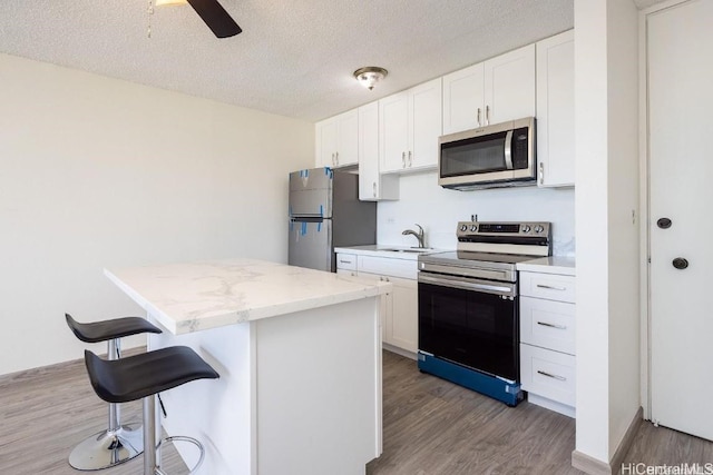 kitchen with white cabinetry, appliances with stainless steel finishes, a breakfast bar, and wood-type flooring