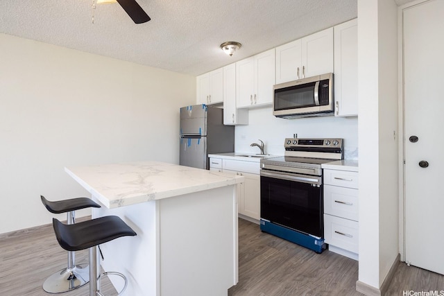 1617 Clark St Unit 702, Honolulu, HI 96822 - kitchen featuring stainless steel appliances, a kitchen island, wood finished floors, a breakfast bar, and white cabinets