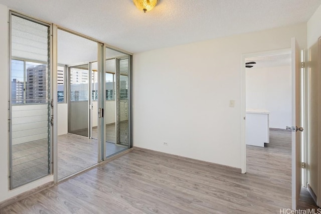 unfurnished room with floor to ceiling windows, a textured ceiling, and light hardwood / wood-style flooring