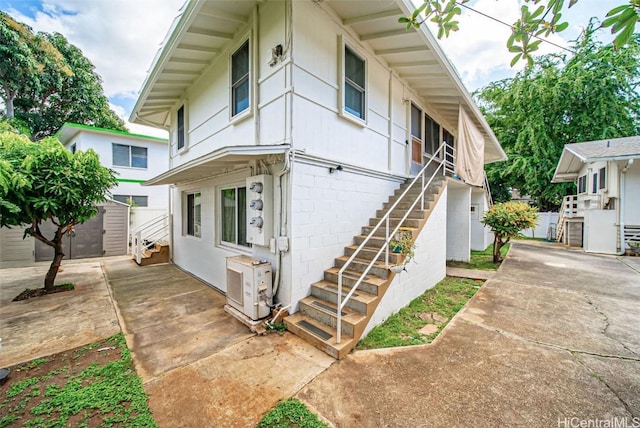 view of front facade featuring an outdoor structure, concrete block siding, fence, stairway, and ac unit