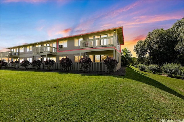 back house at dusk with a balcony and a lawn