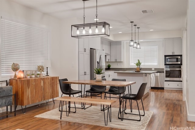 kitchen with stainless steel appliances, hanging light fixtures, hardwood / wood-style flooring, and white cabinets