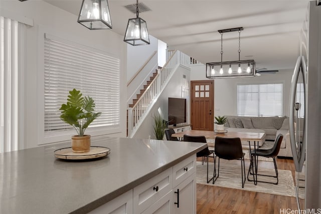 kitchen featuring white cabinetry, hanging light fixtures, light hardwood / wood-style floors, and stainless steel refrigerator