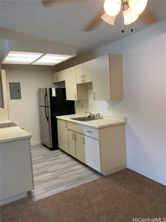 kitchen with ceiling fan, light countertops, electric panel, freestanding refrigerator, and a textured ceiling