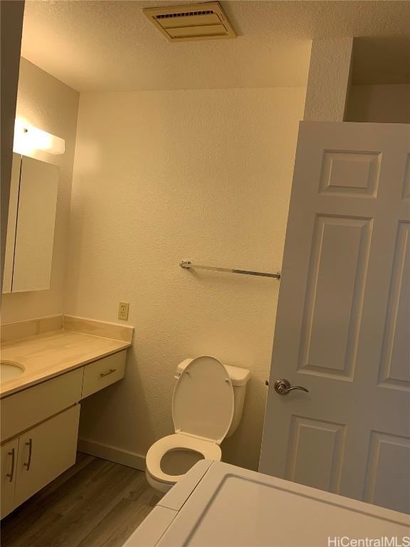 bathroom featuring vanity, wood finished floors, visible vents, and a textured wall