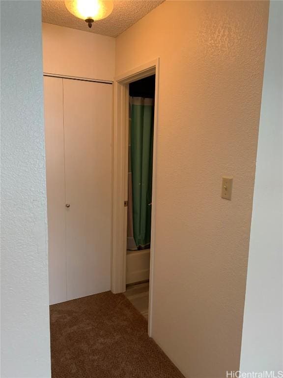 corridor with a textured wall, carpet floors, and a textured ceiling