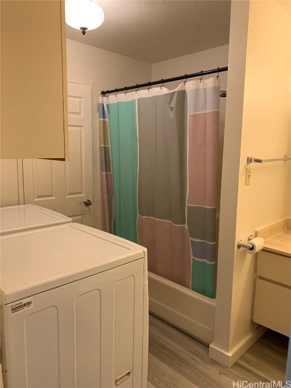 full bathroom with vanity, wood finished floors, washing machine and clothes dryer, a textured ceiling, and shower / tub combo with curtain