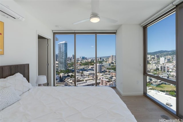 bedroom with hardwood / wood-style flooring, a wall of windows, a wall unit AC, and ceiling fan