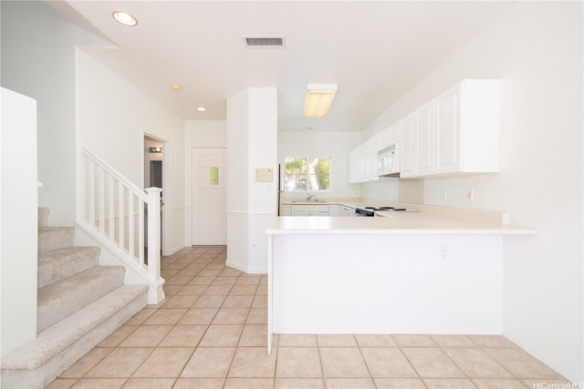 kitchen featuring a peninsula, light tile patterned flooring, white microwave, white cabinetry, and light countertops