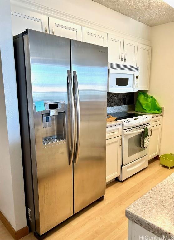 kitchen featuring white appliances, light wood-type flooring, a textured ceiling, and white cabinets