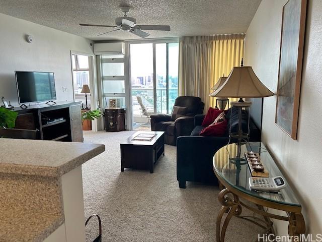 carpeted living room with expansive windows, ceiling fan, a wall mounted air conditioner, and a textured ceiling