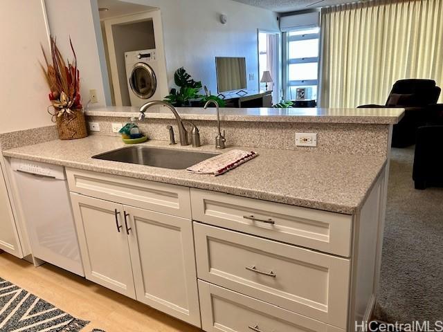 kitchen with white dishwasher, sink, light stone countertops, and white cabinets