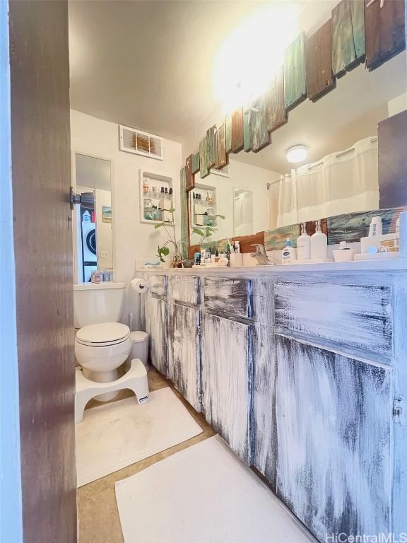 bathroom featuring stacked washer / dryer and toilet