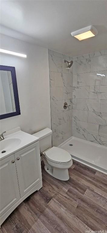 bathroom with wood-type flooring, toilet, vanity, and a tile shower