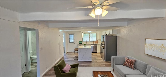 living room featuring sink, beam ceiling, light hardwood / wood-style floors, and ceiling fan