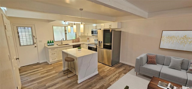 kitchen featuring a kitchen island, appliances with stainless steel finishes, decorative light fixtures, white cabinetry, and a kitchen breakfast bar