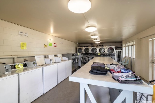 community laundry room featuring concrete block wall, washing machine and dryer, and stacked washer / dryer