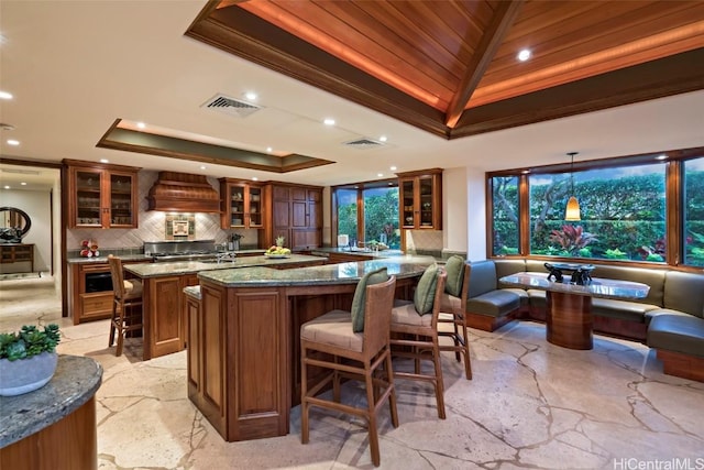 interior space with stone counters, tasteful backsplash, a tray ceiling, custom range hood, and decorative light fixtures