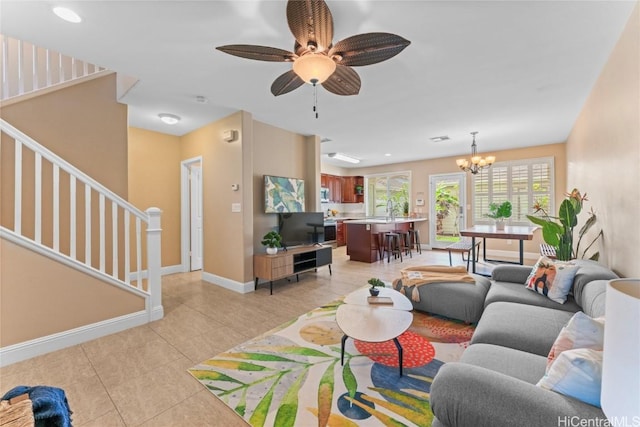 living room featuring light tile patterned floors, stairway, ceiling fan with notable chandelier, and baseboards