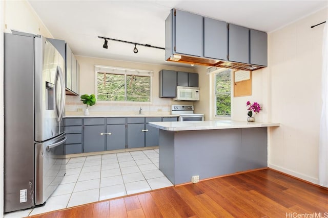 kitchen with stainless steel refrigerator with ice dispenser, stove, a healthy amount of sunlight, and kitchen peninsula