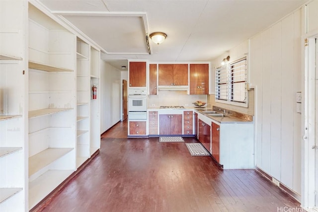 kitchen with brown cabinets, dark wood-type flooring, white oven, light countertops, and under cabinet range hood