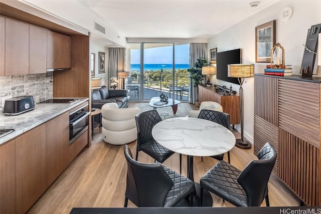 kitchen with light wood-style flooring, a wall of windows, backsplash, and stainless steel oven