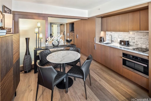 kitchen with stovetop, light wood-type flooring, a sink, and stainless steel oven