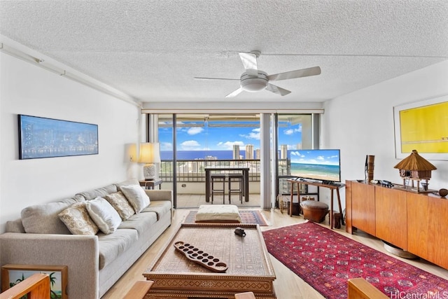 living room with ceiling fan, a textured ceiling, and light hardwood / wood-style flooring