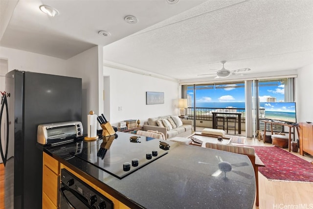 kitchen with hardwood / wood-style flooring, a wall of windows, ceiling fan, black appliances, and a textured ceiling