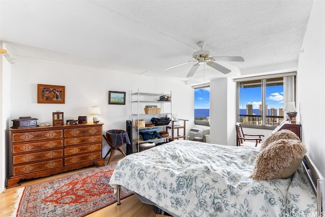 bedroom featuring ceiling fan, hardwood / wood-style flooring, access to outside, and a textured ceiling