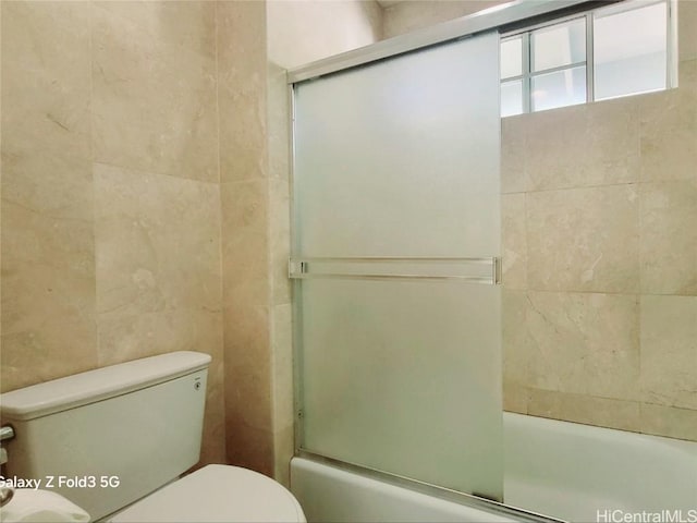 bathroom featuring combined bath / shower with glass door, tile walls, and toilet