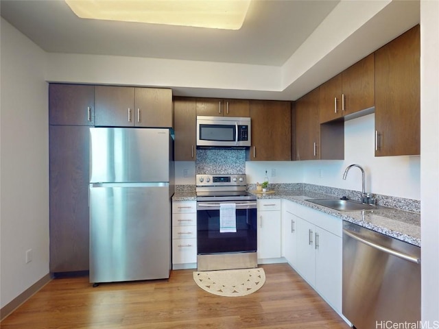 kitchen with sink, appliances with stainless steel finishes, light stone counters, tasteful backsplash, and light hardwood / wood-style floors