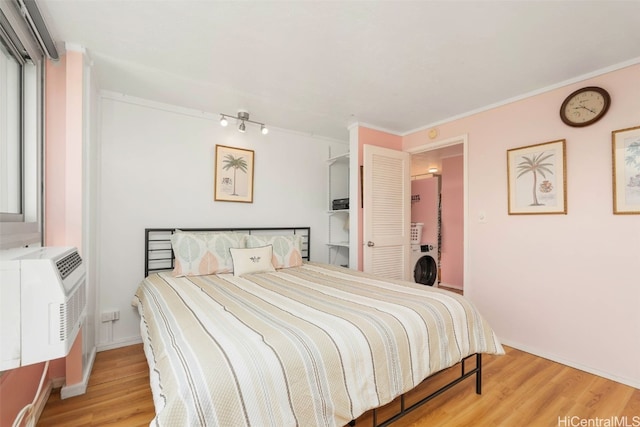 bedroom featuring ornamental molding, a wall mounted air conditioner, wood finished floors, and washer / dryer