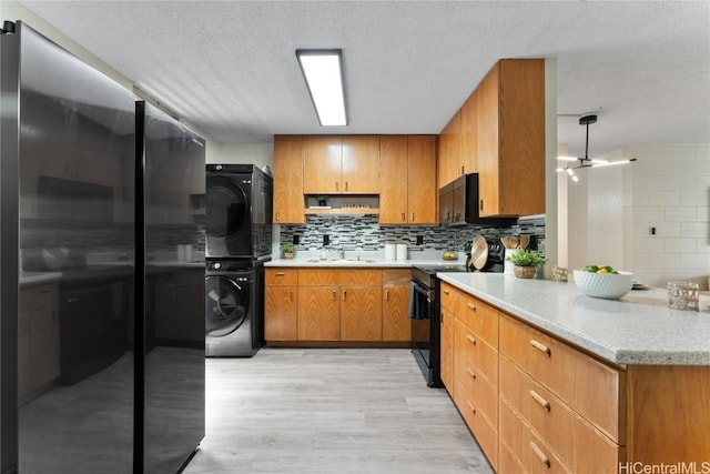 kitchen featuring sink, stacked washer / dryer, black / electric stove, decorative backsplash, and light wood-type flooring