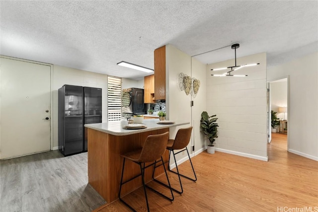 kitchen featuring light wood-type flooring, a kitchen bar, kitchen peninsula, black fridge, and a textured ceiling